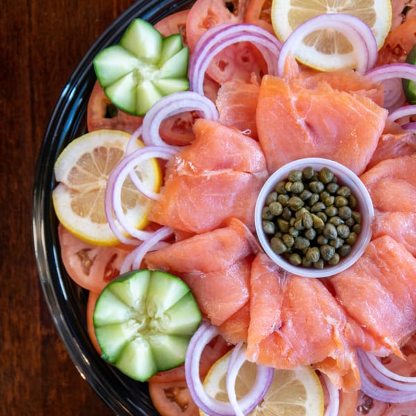 Smoked salmon platter with capers, sliced tomatoes, red onions, lemons, and cucumber slices.