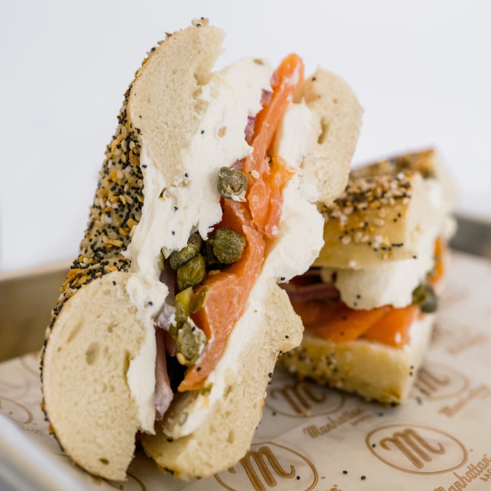 Everything bagel with cream cheese, smoked salmon, and capers on branded parchment paper.