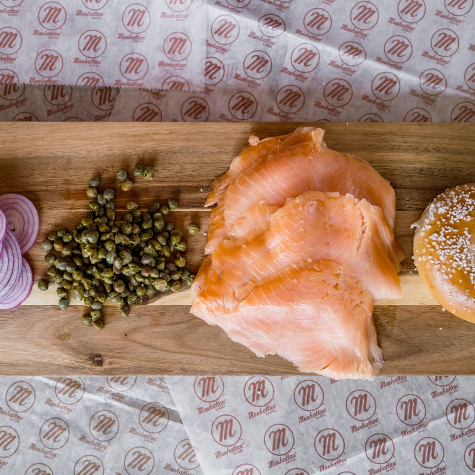 Smoked salmon, capers, red onion, and a bagel with salt on a wooden board.