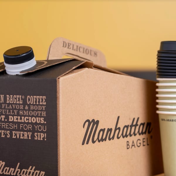 Manhattan Bagel coffee box with a black cap and a stack of disposable coffee cups.