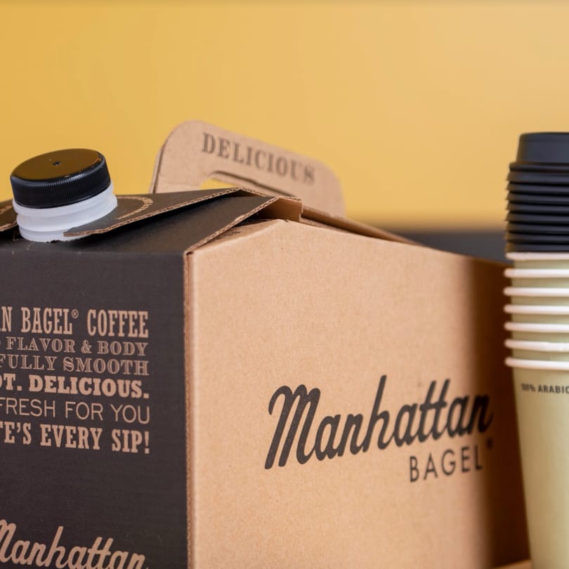 Manhattan Bagel coffee box with a black cap and a stack of disposable coffee cups.