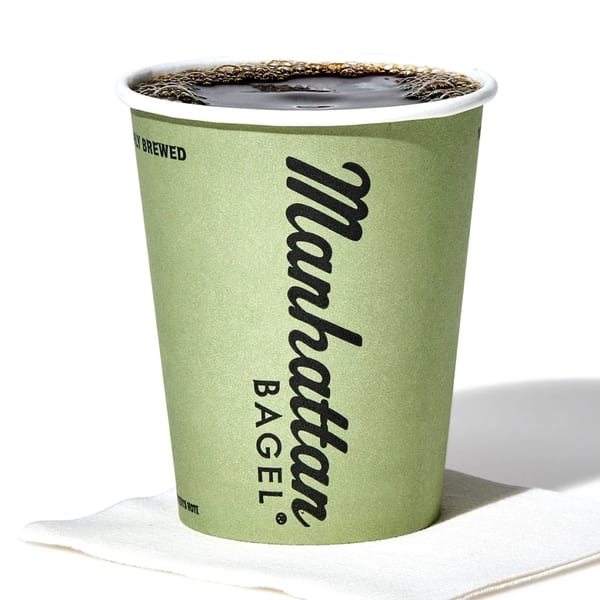 A green Manhattan Bagel coffee cup filled with dark coffee, sitting on a white napkin.