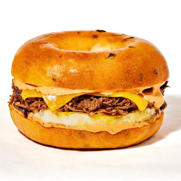 Manhattan Bagel with shredded meat, melted cheese, egg, and creamy sauce on a white background.
