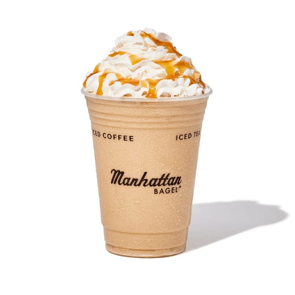 Manhattan Bagel's iced coffee with whipped cream and caramel drizzle in a clear plastic cup.