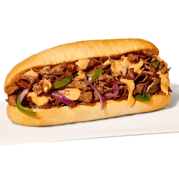 A Manhattan Bagel cheesesteak sandwich with steak, green peppers, red onions, and cheese sauce.