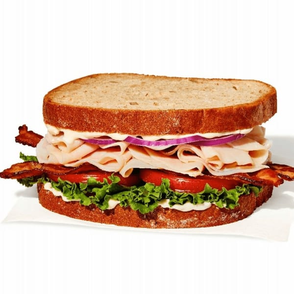 A turkey, bacon, lettuce, tomato, red onion, and mayonnaise sandwich on toasted bread.