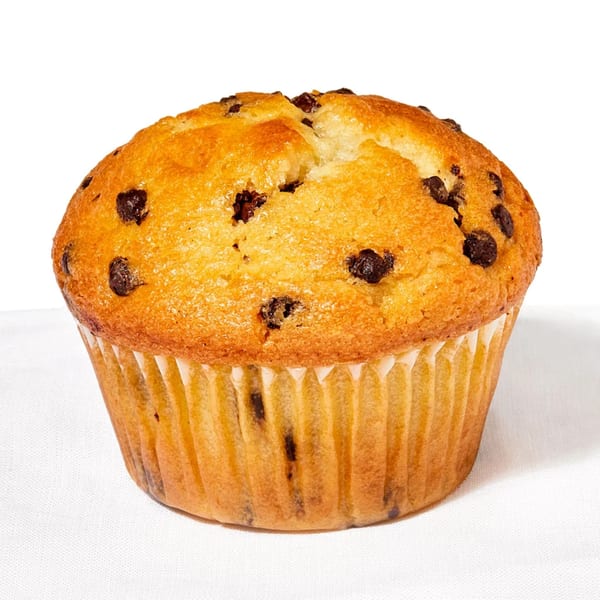 A golden-brown chocolate chip muffin in a paper liner sits on a white surface.
