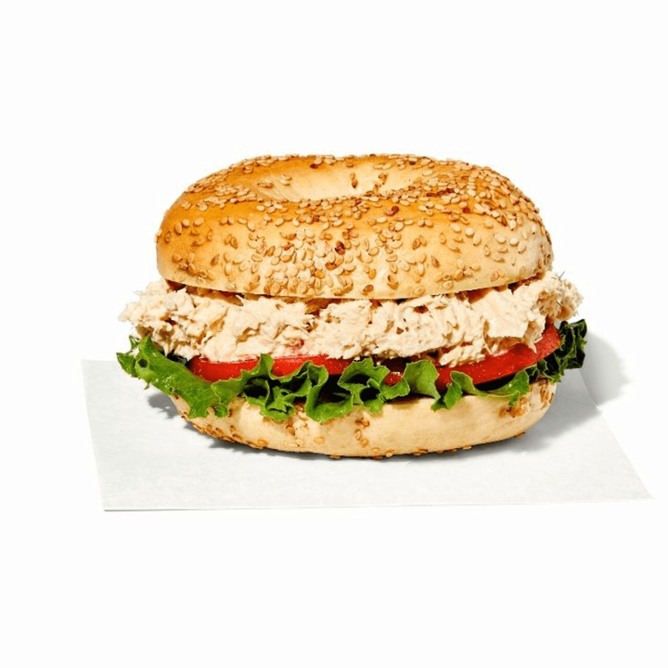 Manhattan Bagel's tuna salad bagel sandwich with lettuce and tomato on a white background.