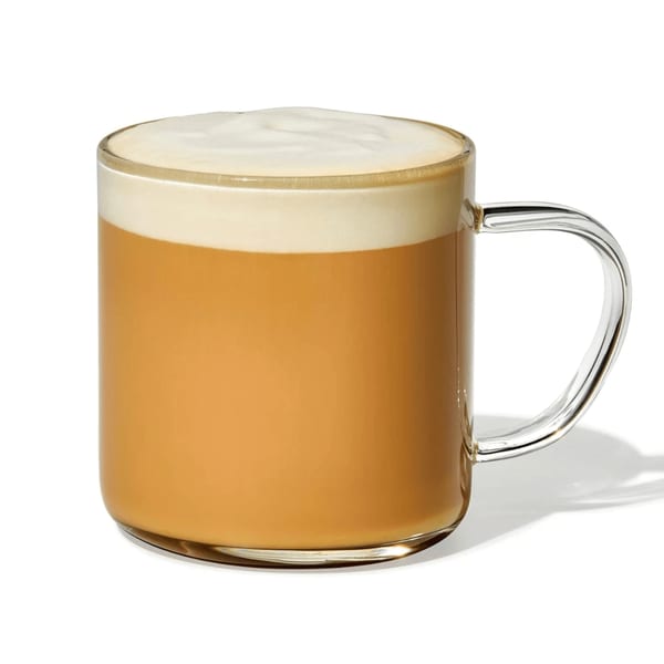 A Manhattan Bagel latte in a clear glass mug with a thick layer of foam.