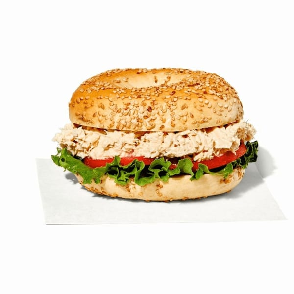 Manhattan Bagel's tuna salad bagel sandwich with lettuce and tomato on a white background.